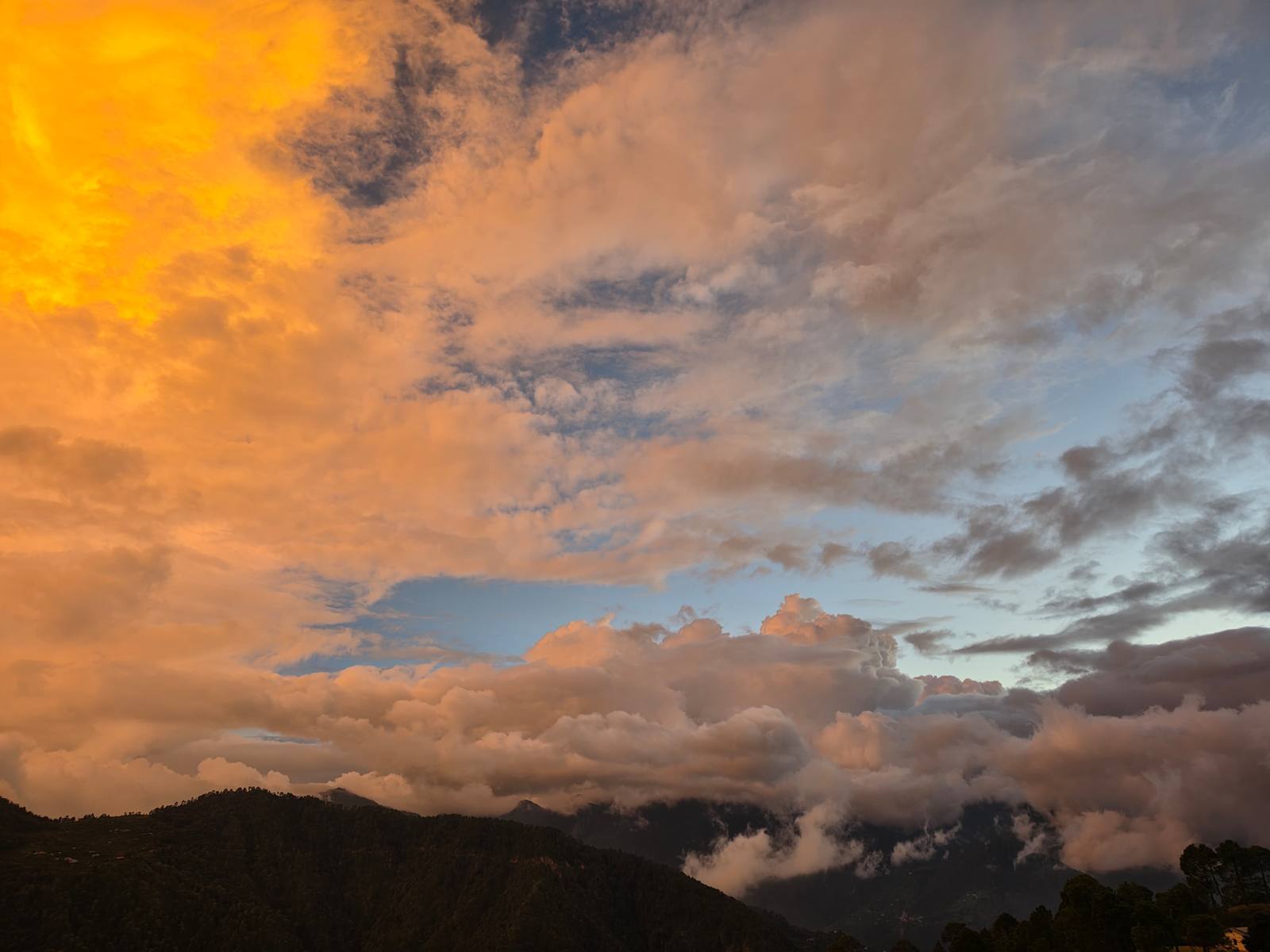 A dramatic orange sunset lighting up clouds over the Kumaon ridgelines